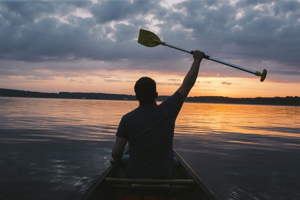 silhouette of man holding up paddle on lake during sunset